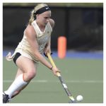 a young woman outdoors playing field hockey focused intently on the game