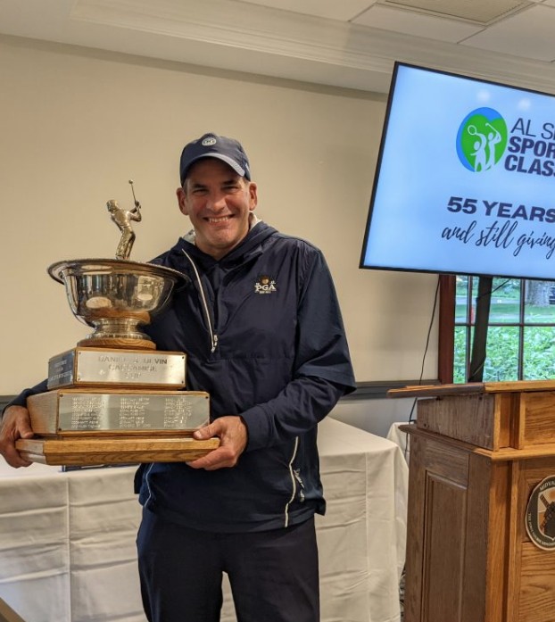 a smiling man holding a large trophy with many names engraved along the base