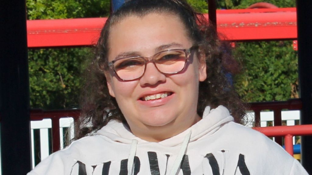 a smiling woman with brown curly hair and glasses wearing a white Nirvana sweatshirt