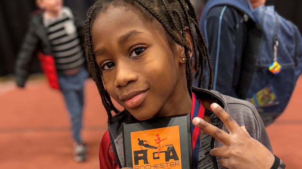 a boy with a confident smile and braids holds an award proudly under his chin