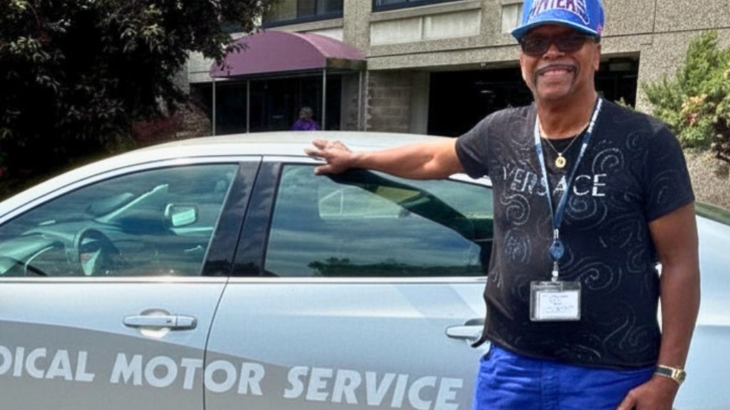a smiling man standing in front of a car
