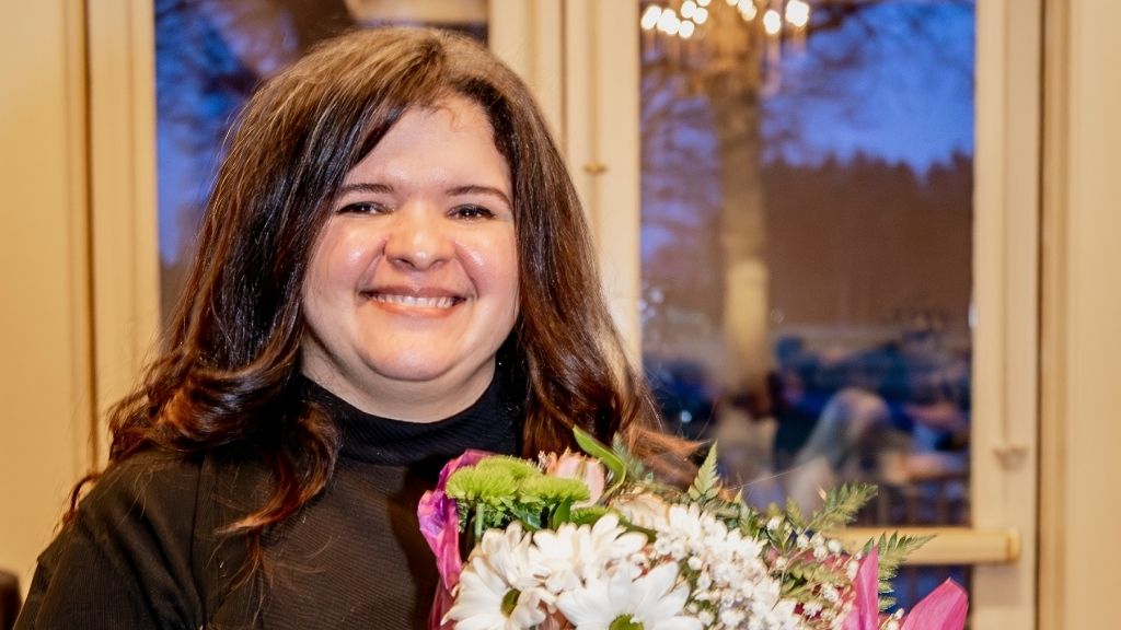 a woman with shoulder length brown hair smiles holding a bouquet of flowers